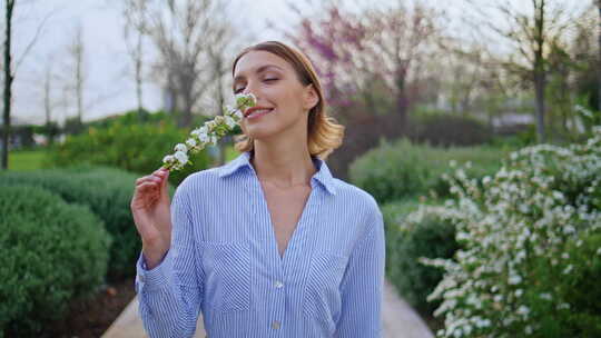 美丽的女孩嗅着花站在风景如画的花园特写快