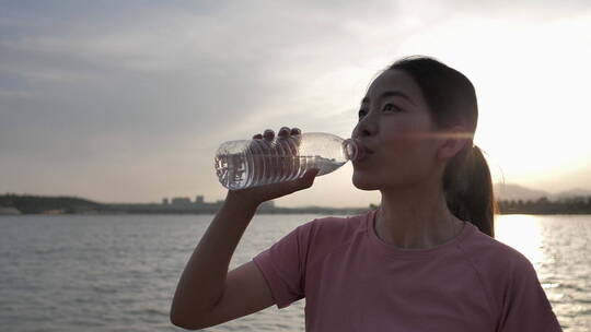 夕阳下中国女性运动后在河边喝水