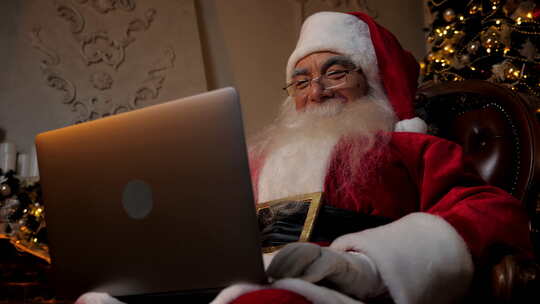 微笑的现代圣诞老人使用笔记本电脑为儿童填