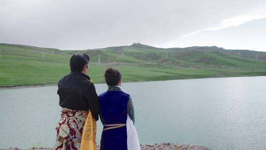 穿少数民族服饰的男女眺望远方湖泊和输电塔