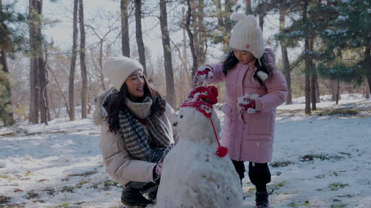 年轻妈妈和女儿在雪地里堆雪人