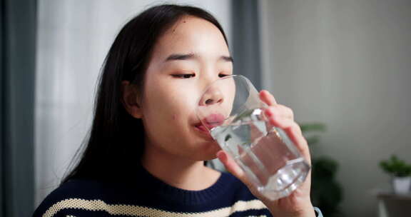 年轻的亚洲女人在家里的餐桌上享受喝水。