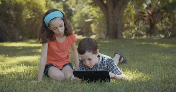 姐姐和弟弟趴在草地上玩电脑