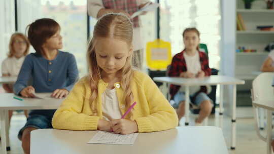 美丽的长发金发学生坐在学校的书桌前，填写