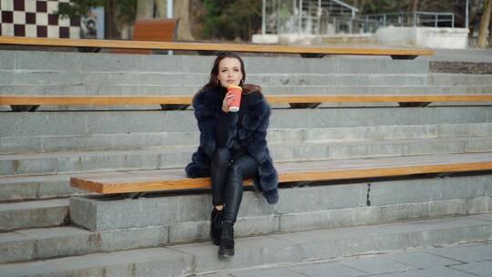 坐在长椅上喝咖啡的女人