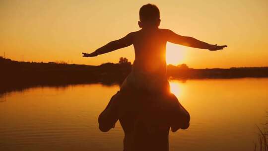 落日夕阳下湖边父亲用肩膀托起儿子的剪影
