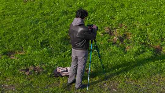 摄影师男子在草地上设置相机三脚架-广角镜