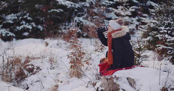 一个女人坐在石头上，在雪地里用烧瓶喝水