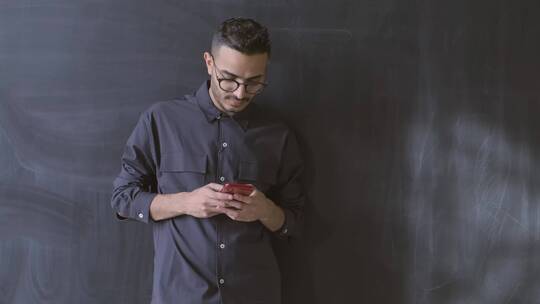 一个男人站在黑板前低头看手机