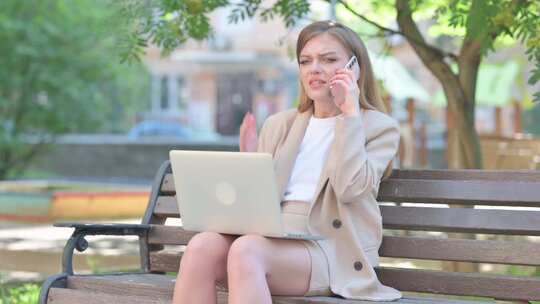 愤怒的女商人在电话上打架并在户外使用笔记