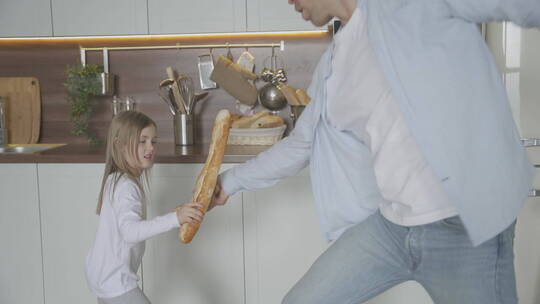 在厨房里和女孩拿面包棒玩耍的父亲