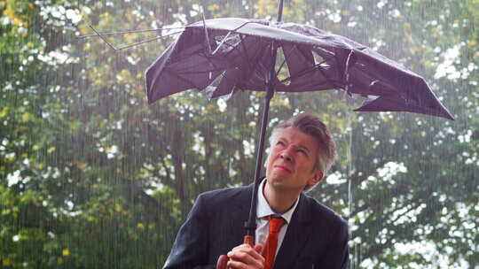 雨中商人躲在破雨伞下