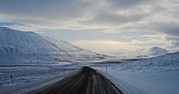 在午夜的阳光下，沿着冰岛一条荒芜、白雪覆盖的山路行驶。