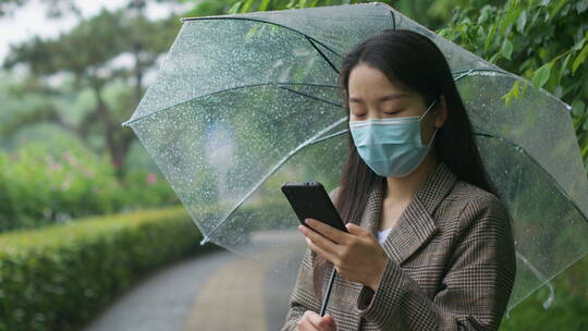 中国女性打伞步行踏春打电话等公交玩手机