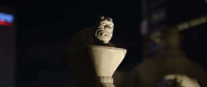 夜晚，灯光照在建筑物附近的东方石龙雕塑上