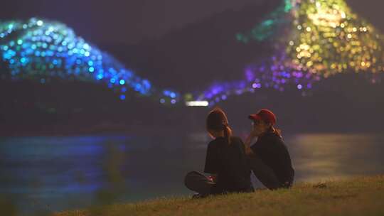 两个女孩坐在江边看夜景