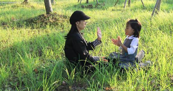 妈妈与女儿坐在阳光草地上拍手玩耍