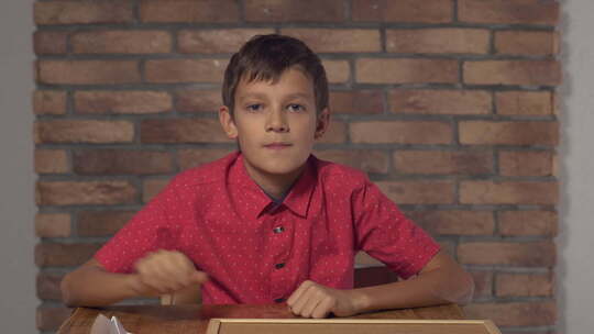 坐在书桌前的孩子拿着背景红砖墙上有字母旅行的挂图