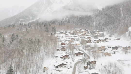 无人机镜头从下雪的滑雪村下降，雪带着低沉的云层飞向相机