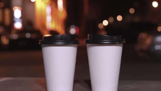 模糊城市灯光背景下的一次性纸杯和热咖啡