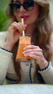 女人在外面的咖啡馆用吸管喝橙汁。垂直