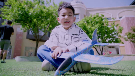 快乐的小男孩坐在草地上玩飞机