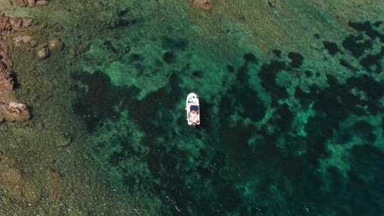 漂浮在蓝色海浪和红色岩石中间的白色船只的空中俯视图