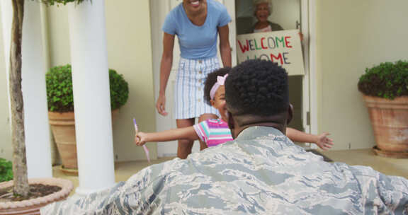 非裔美国男士兵用美国国旗拥抱他微笑的妻子和女儿
