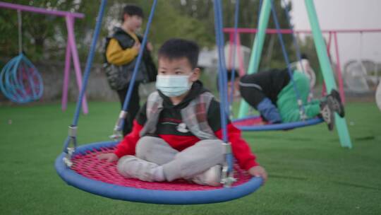 带着口罩的小男孩盘腿坐在秋千上玩耍视频素材模板下载