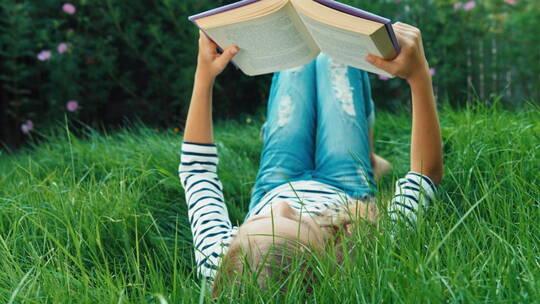 快乐的女孩躺在草地上阅读书籍