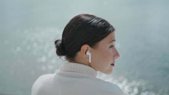 坐在湖水特写镜头前戴着无线耳塞听音乐的女游客