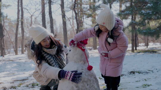 年轻妈妈和女儿在雪地里堆雪人