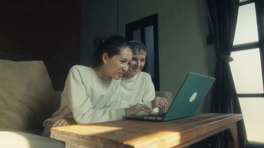 两个年轻女人在家一起放松时在笔记本电脑上看有趣的视频