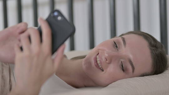 年轻女子在床上使用智能手机视频素材模板下载