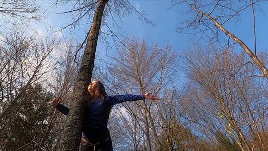 女人双臂摊开倚在树干上