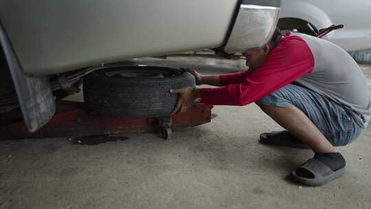 年轻的亚洲机械师在汽车下面放了一个轮子视频素材模板下载