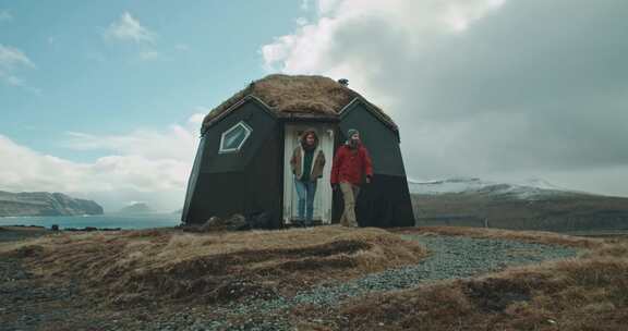 一男一女从雪山附近的小湖边小屋走出来