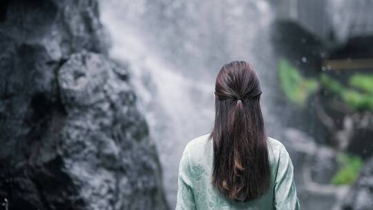 身穿汉服年轻女子在园林景观水景墙前摇扇子