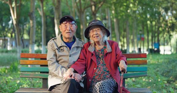 幸福的老年夫妇坐在公园长椅上面带笑容聊天