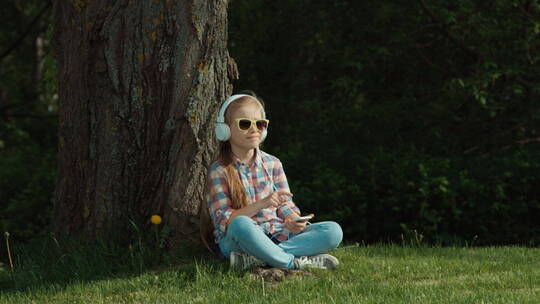 女孩坐在树下戴着耳机听音乐