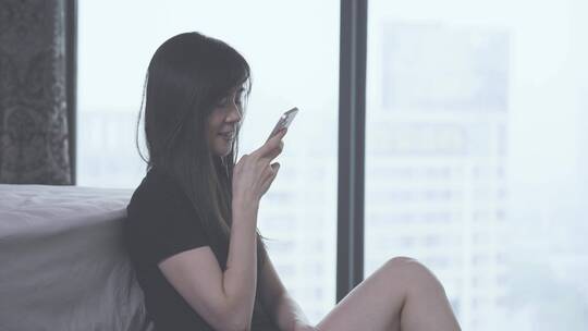 女孩开心地坐在窗边对着手机说语音