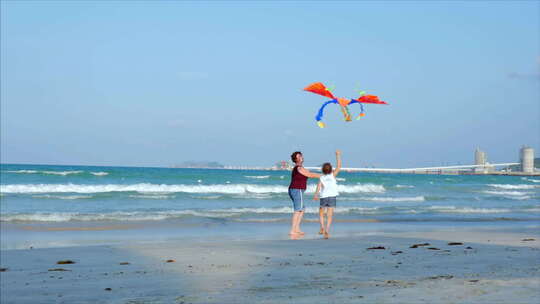 快乐的祖母带着孩子玩风筝，一家人在热带沙滩上奔跑