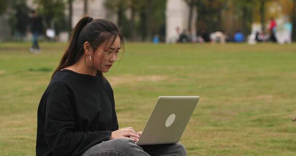 一位女大学生坐在校园草地上用笔记本电脑