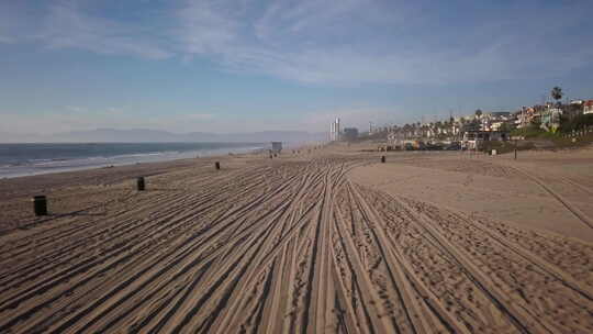 黄金时段的空中拍摄，在曼哈顿海滩的沙滩上向后移动，露出汽车印记