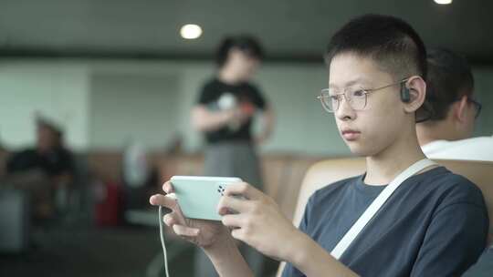 男孩暑假出游在机场候机大厅玩手机游戏