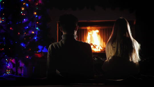 两个青少年坐在圣诞树附近的壁炉前