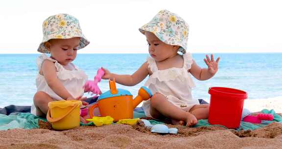 双胞胎女婴坐在海滩上玩沙子