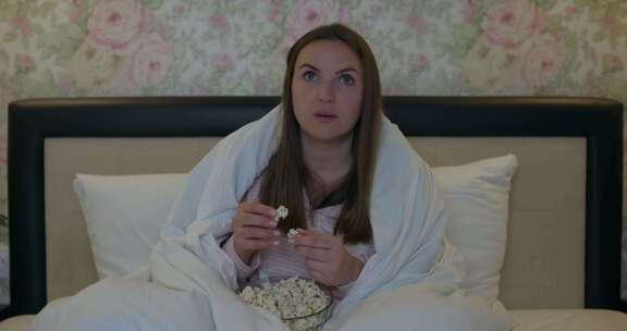 一个快乐的女人在床上吃爆米花时享受电视上