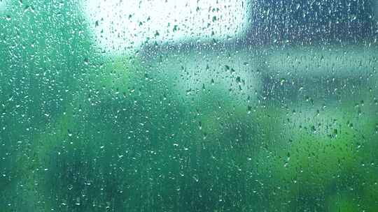 雨水落在窗户玻璃上窗外绿色背景的治愈氛围