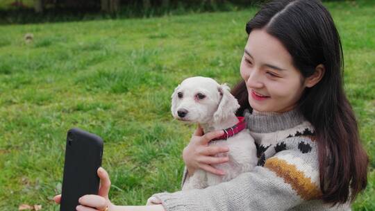 女孩抱着宠物犬在公园里玩耍用手机自拍